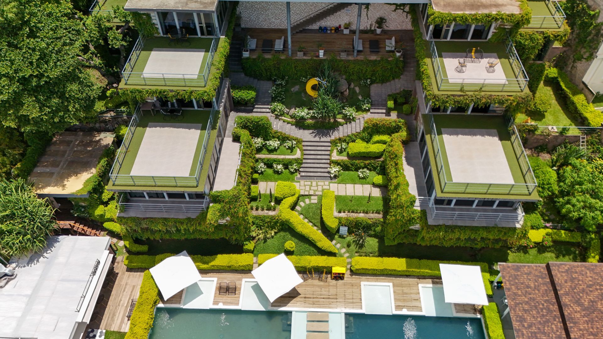 Vista aérea de residence cardedeu coatepeque con setos geométricos, escalones y una piscina en la parte inferior.