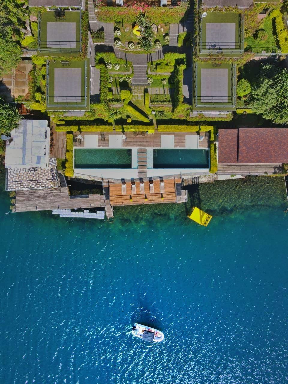 Vista aérea de una villa frente al mar con piscinas, un jardín exuberante, un muelle y un pequeño barco en aguas de un azul brillante en hotel cardedeu coatepeque
