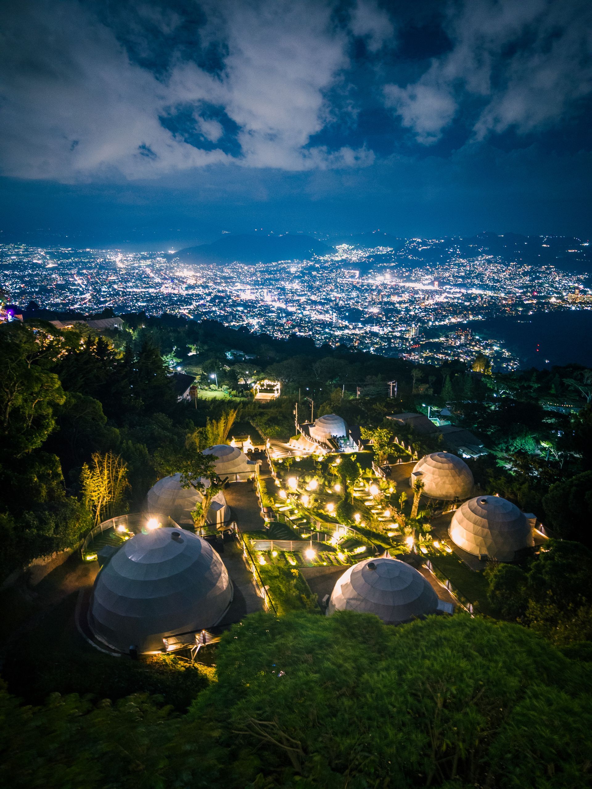 Vista nocturna de una ciudad en la ladera de una colina con luces brillantes y edificios con forma de cúpula en primer plano el boquerón