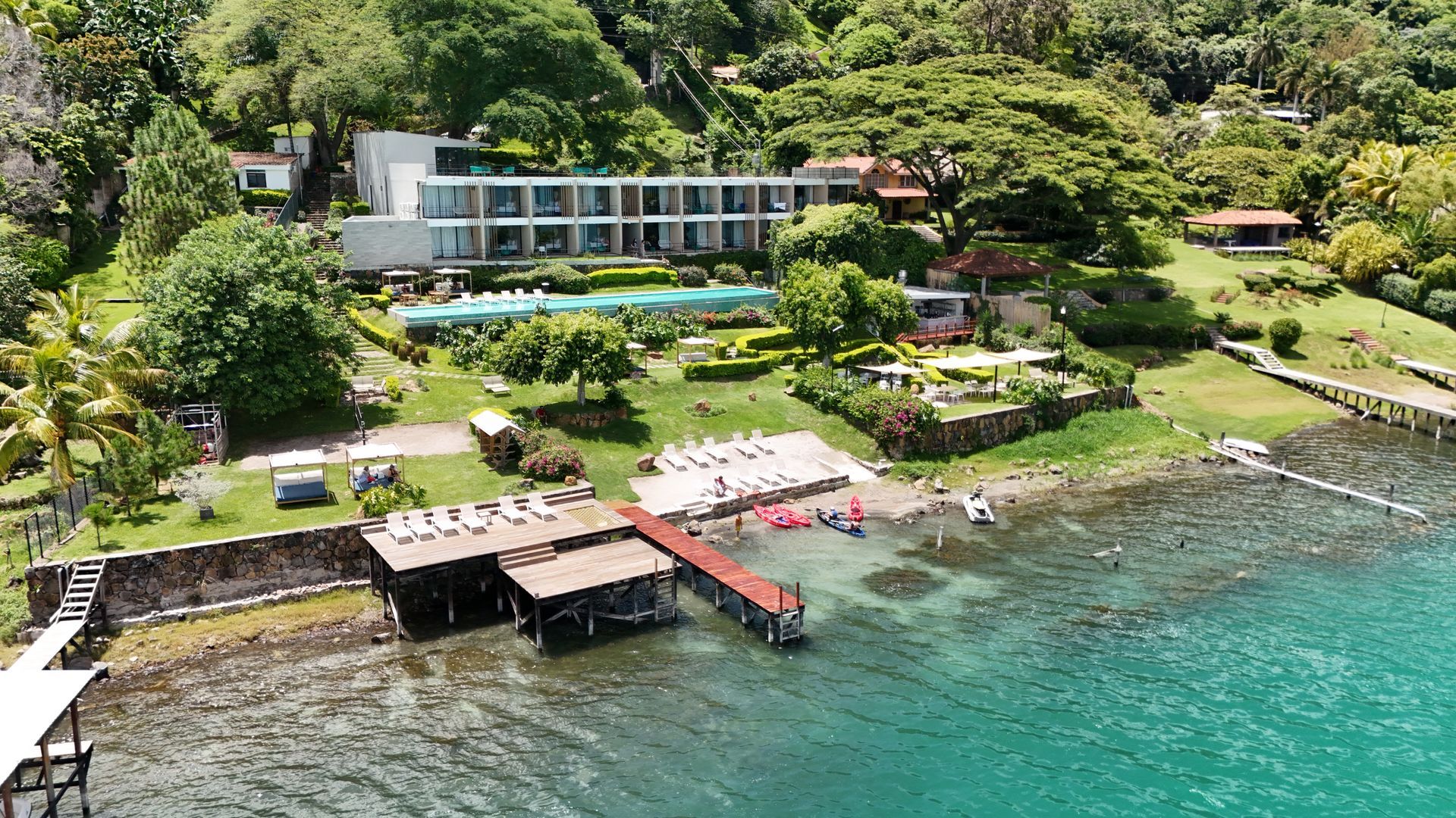 hotel cardedeu coatepeque con edificios blancos, exuberante vegetación, muelles y aguas turquesas.