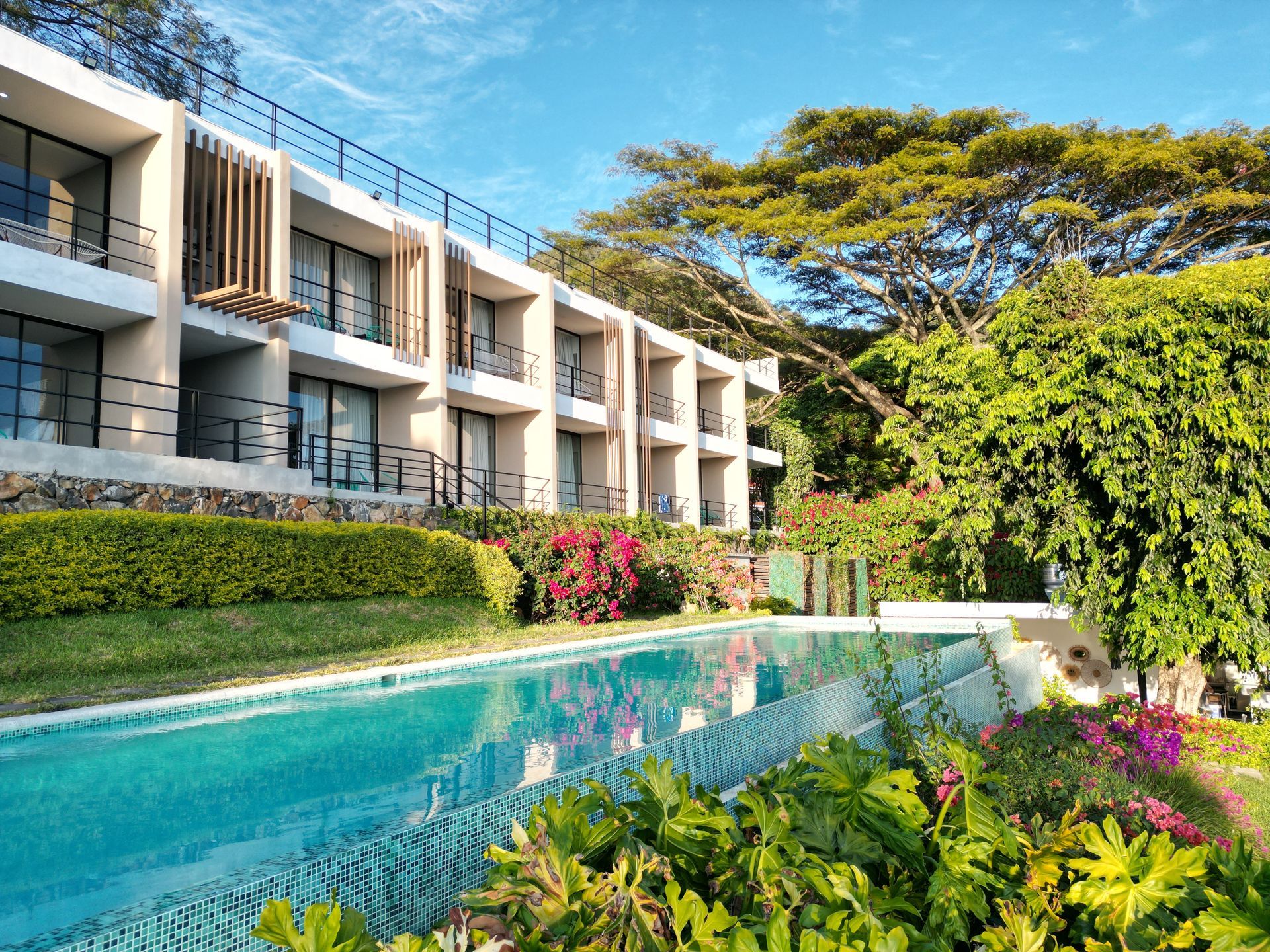 Piscina de cardedeu hotel coatepeque, con exuberante vegetación y flores brillantes bajo un cielo despejado.