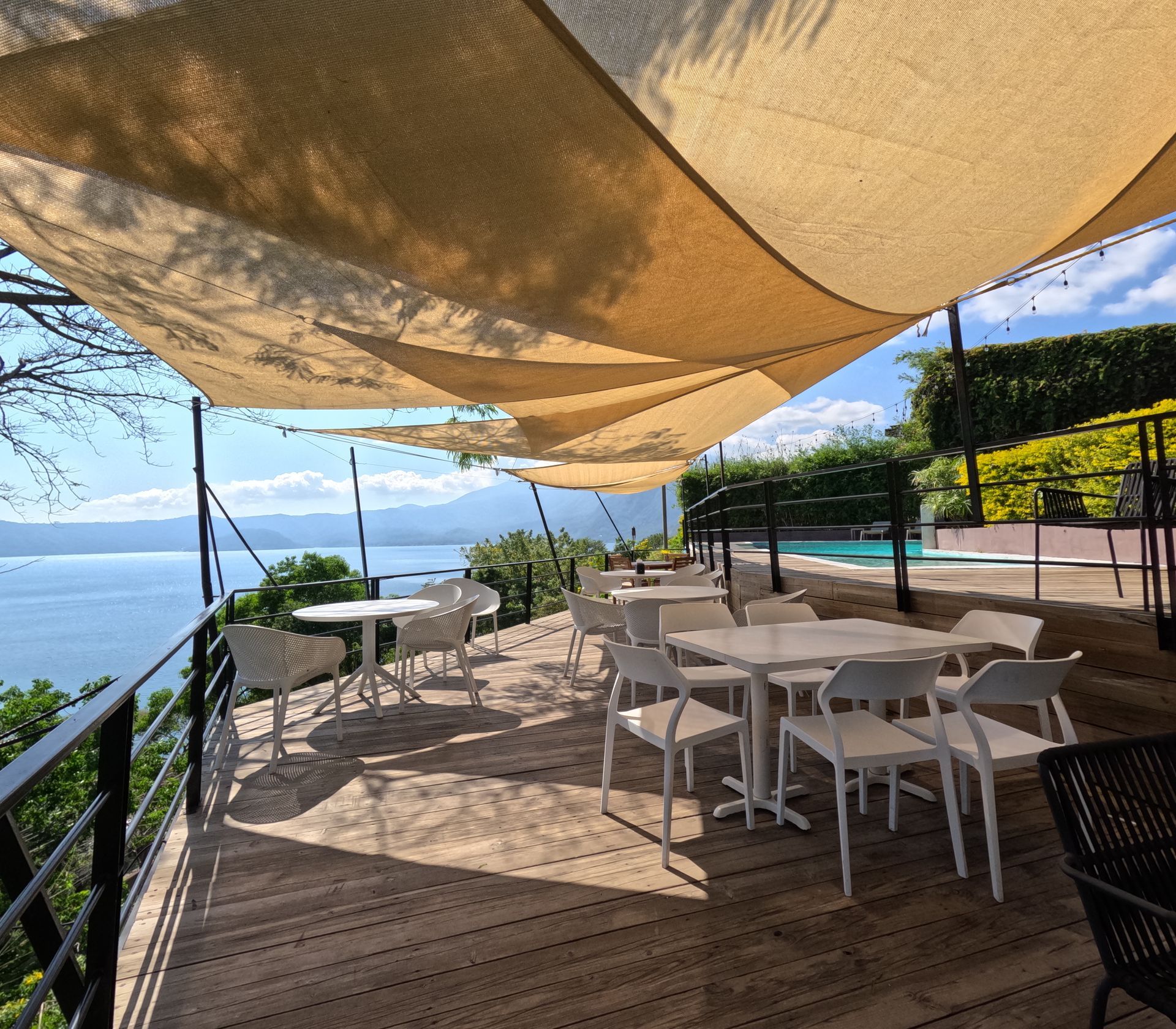 Terraza sombreada de una cafetería junto al mar, con mesas y sillas blancas con vistas al océano en cardedu hotel coatepeque