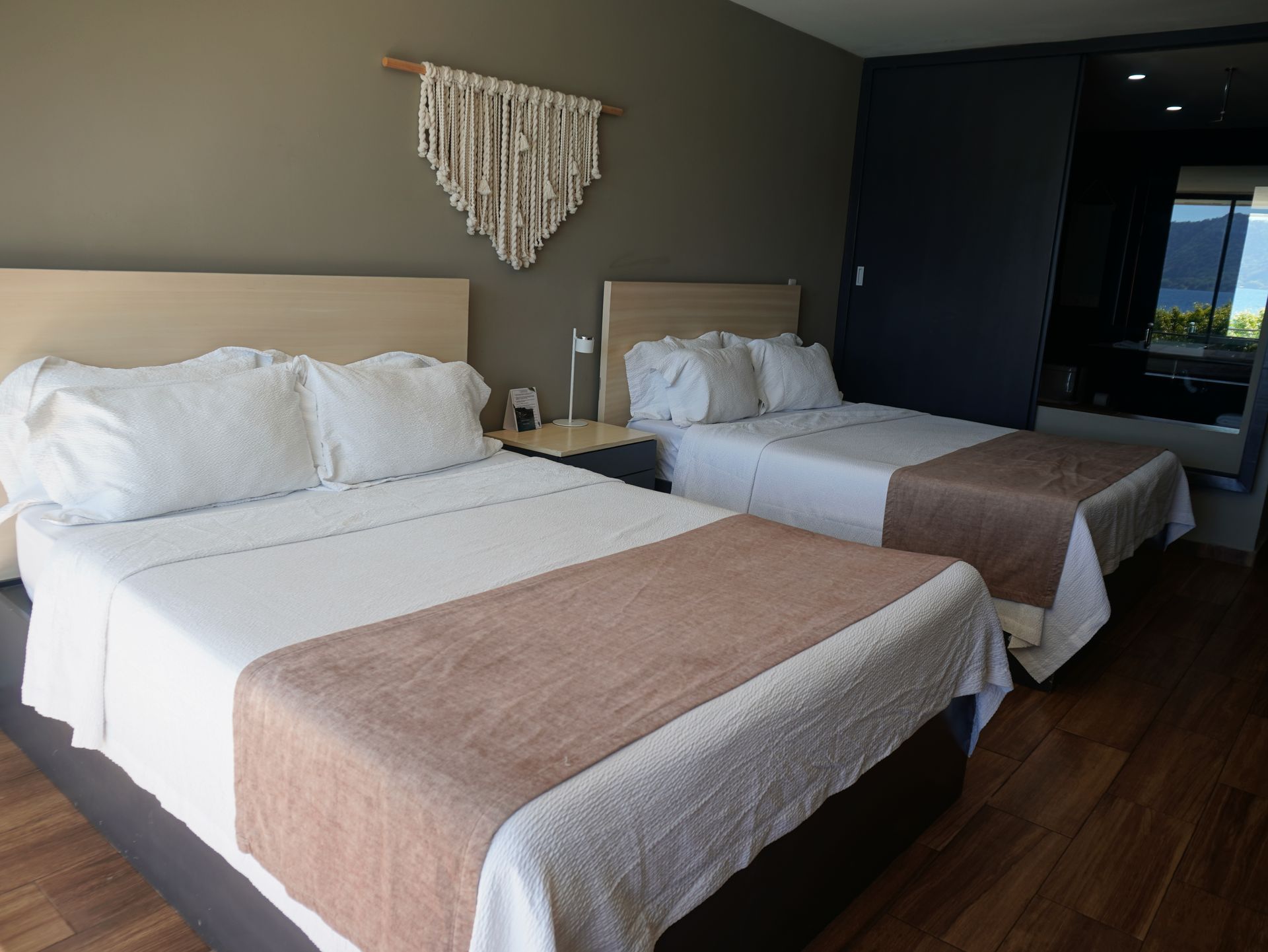 Dos camas impecablemente hechas en una moderna habitación de hotel con mantas beige y suelo de madera en el hotel cardedeu coatepeque