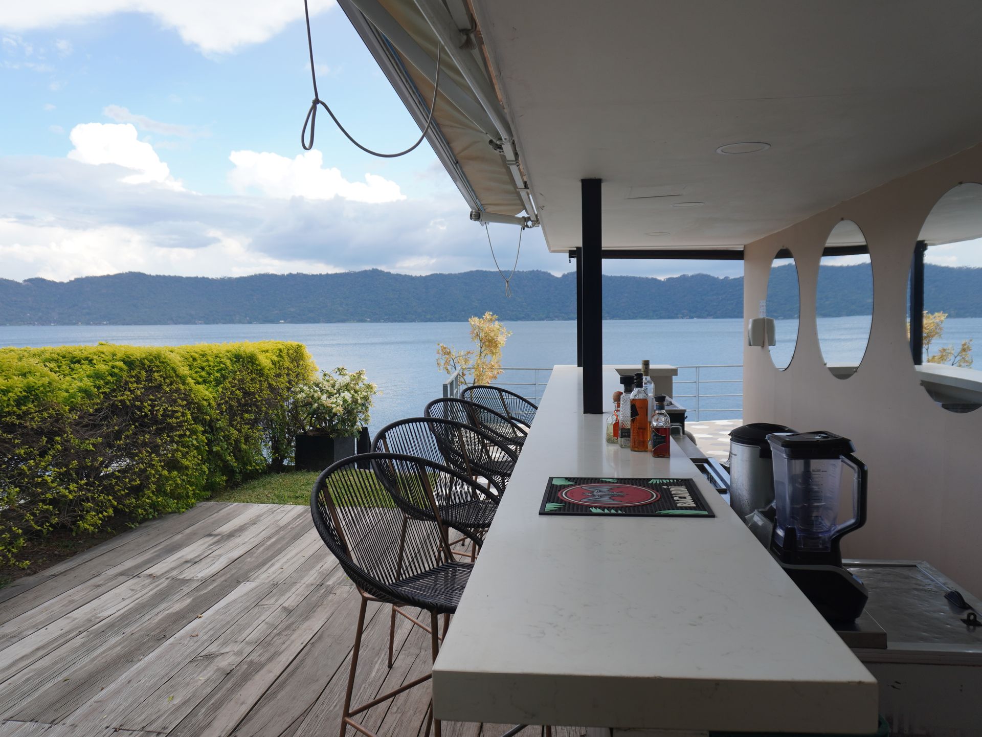 Patio cubierto frente al lago con mesa de bar, sillas y vista al lago al atardecer.