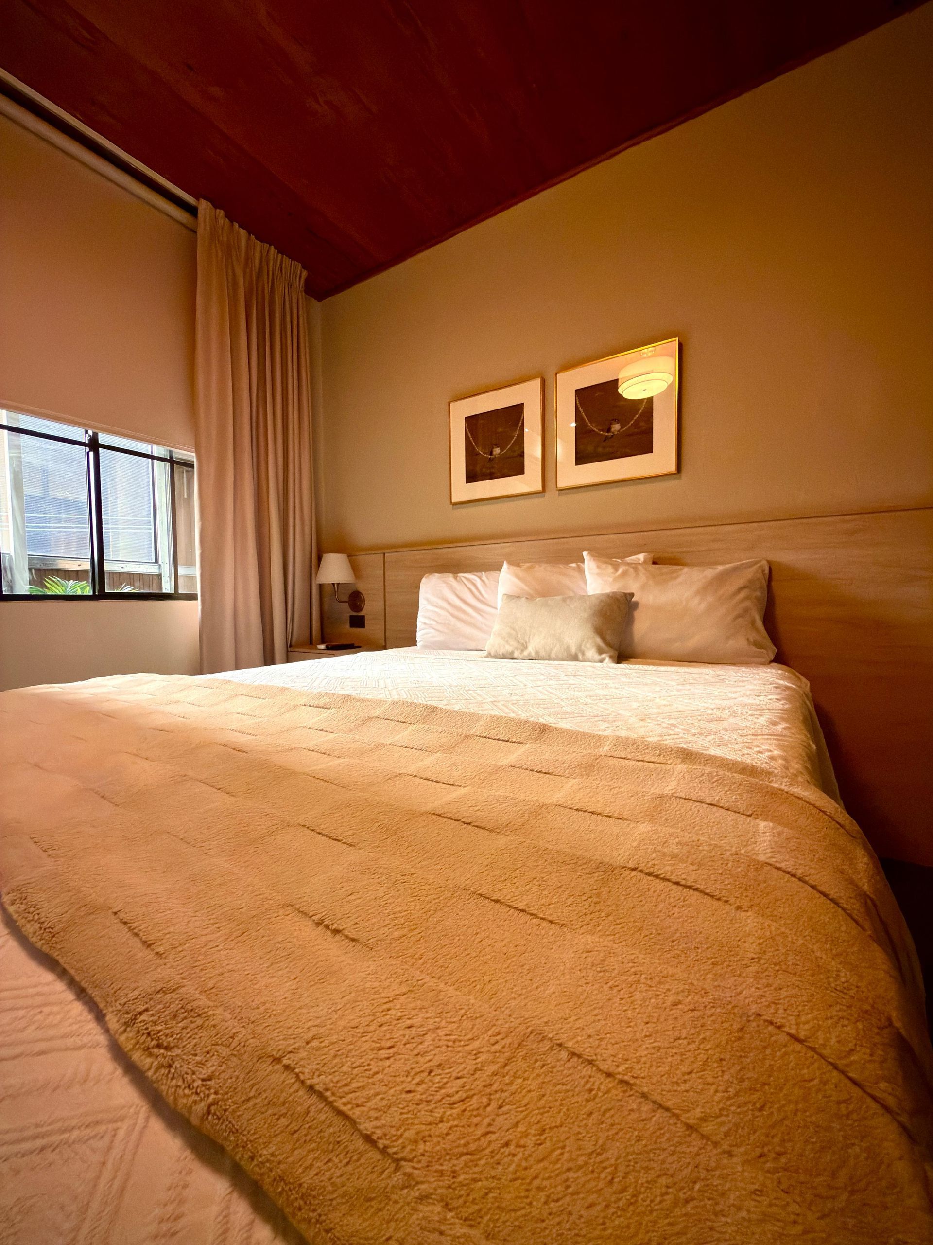 Habitación acogedora con una cama grande, ropa de cama beige, cuadros en la pared y una ventana con vistas en hotel cardedeu suites
