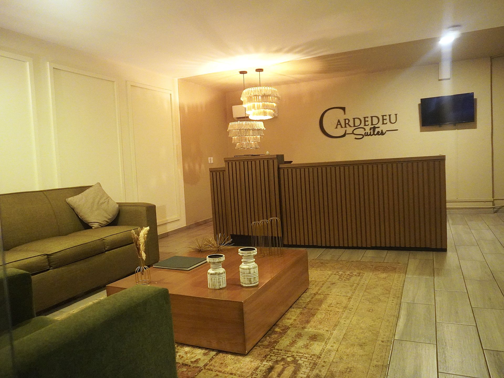 Vestíbulo de hotel moderno con sofás verdes, mesa de centro de madera, mostrador de recepción e iluminación cálida en hotel cardedeu suites