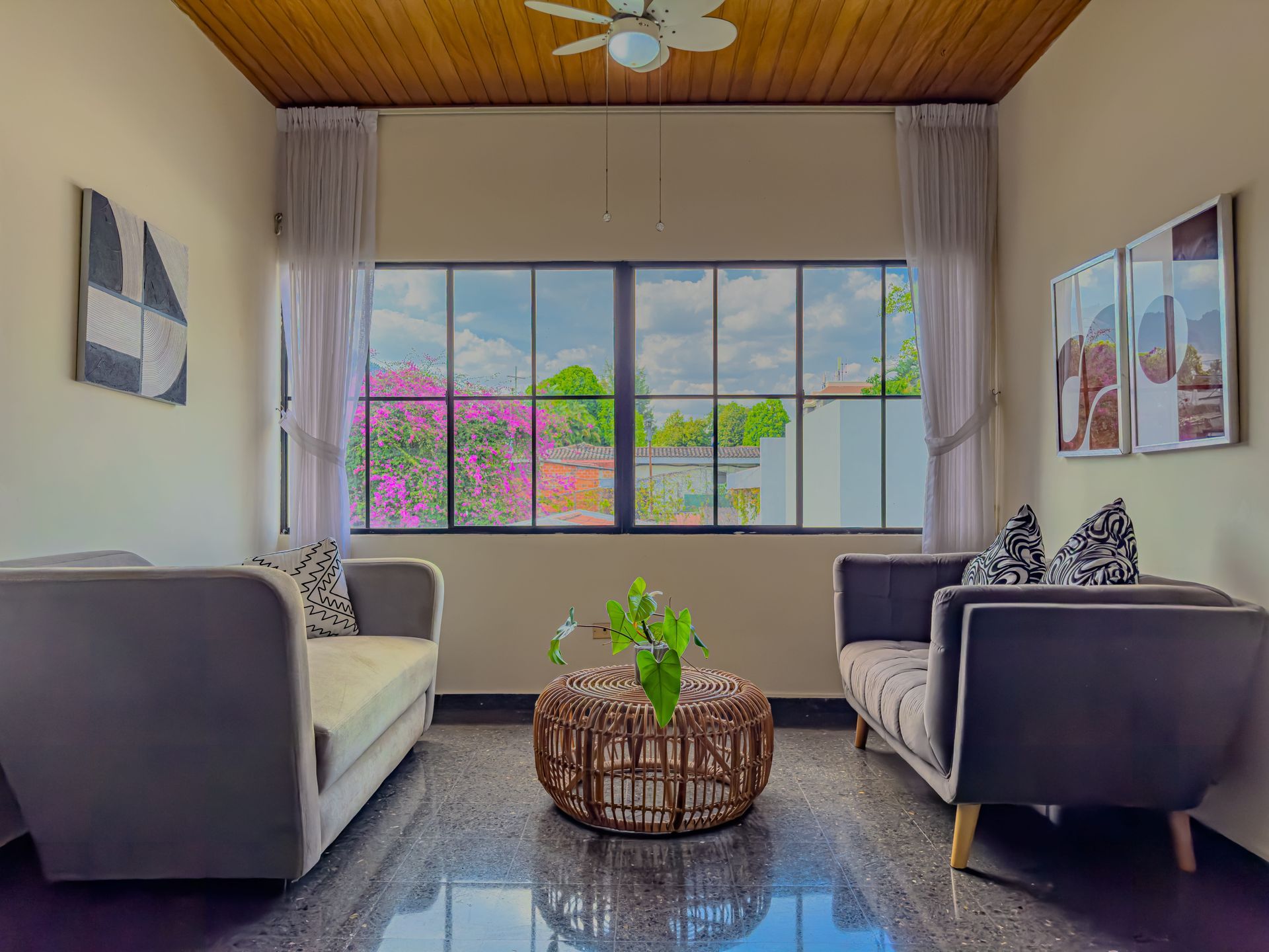 Luminoso salón con dos sofás, mesa de centro de mimbre y una gran ventana con vistas a árboles y flores en hotel cardedeu suites