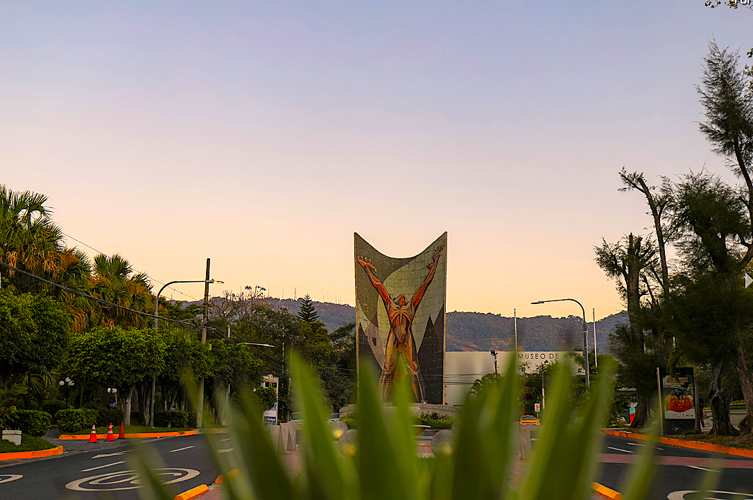 Jardín al atardecer con una colorida escultura en forma de mariposa y plantas verdes en primer plano.