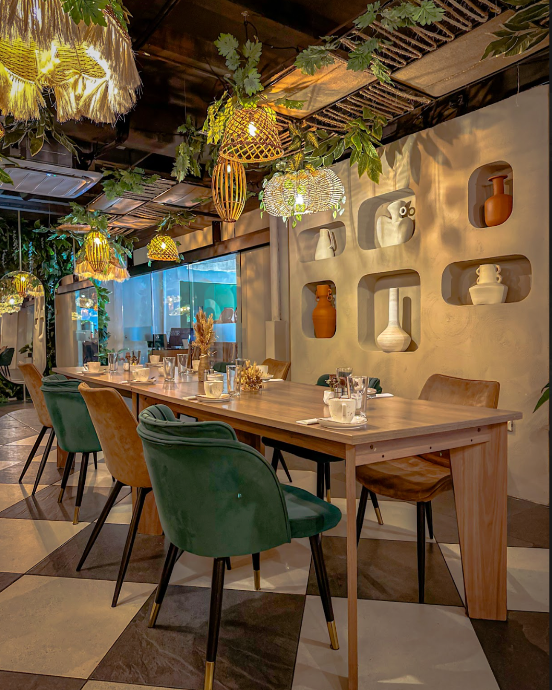 Elegante zona de comedor de restaurante con mesas de madera, sillas verdes, plantas colgantes y una iluminación cálida y suave.