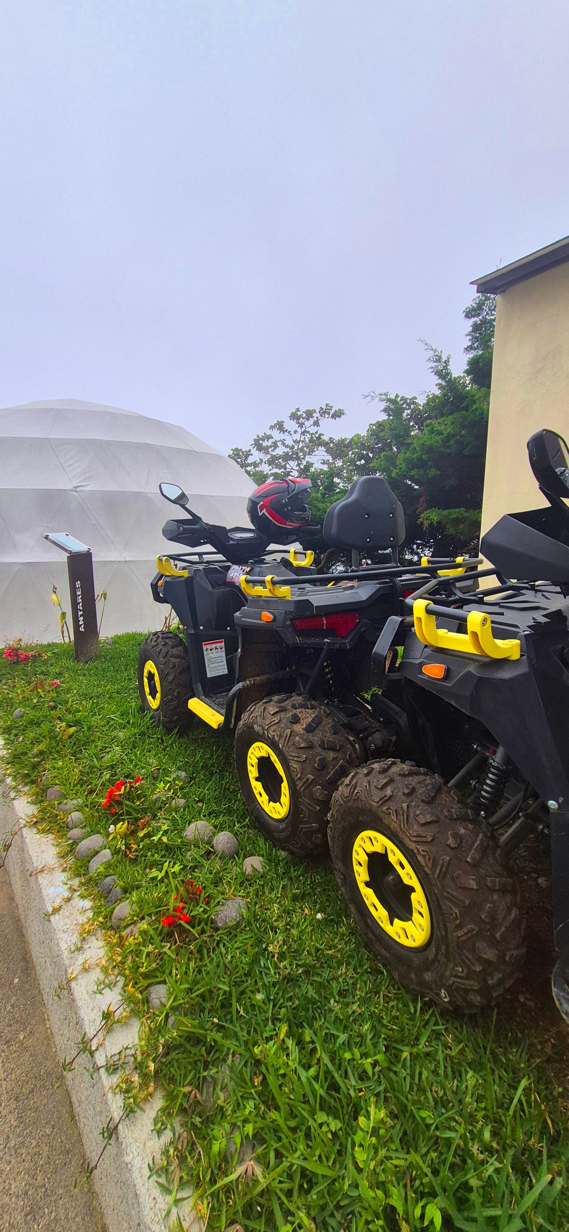 Un quad negro con llantas amarillas aparcado en la hierba mojada junto a un edificio durante la lluvia.