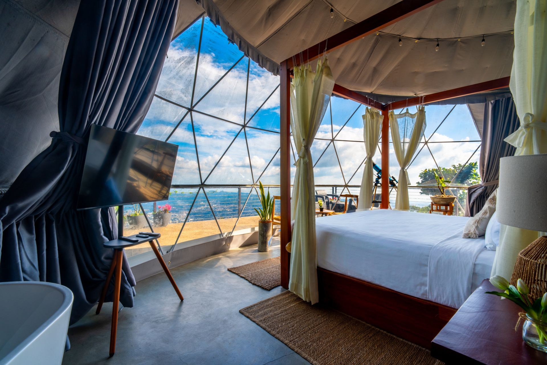 Habitación tipo tienda de campaña con vistas al océano, cama con dosel, cortinas azules y balcón con vistas al mar.