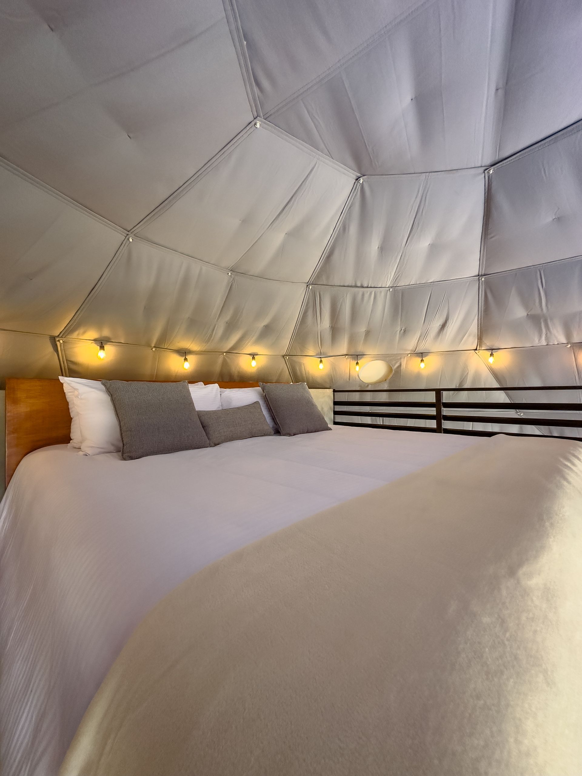 Cama acogedora bajo un techo abovedado blanco acolchado con luces de guirnalda cálidas y almohadas.