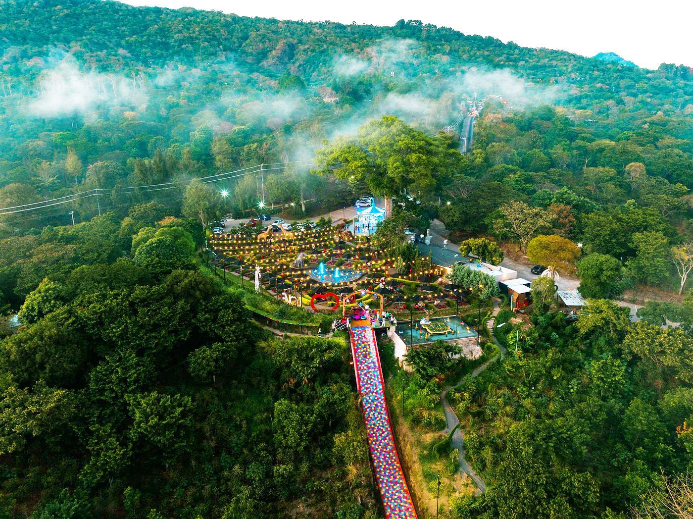 Vista aérea de un colorido complejo de templos en la ladera de una colina, en medio de un frondoso bosque verde y montañas envueltas en niebla.
