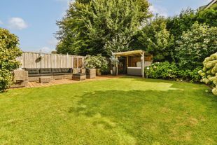 Backyard with green lawn, wooden fence, trees, and a small patio shelter