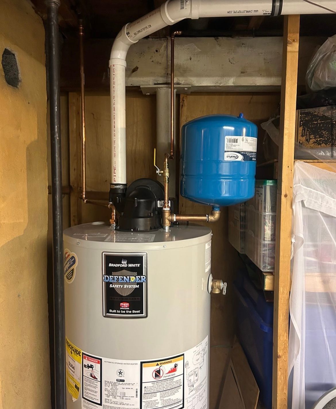 Water heater with copper pipes, a blue expansion tank, and white PVC in a utility room.