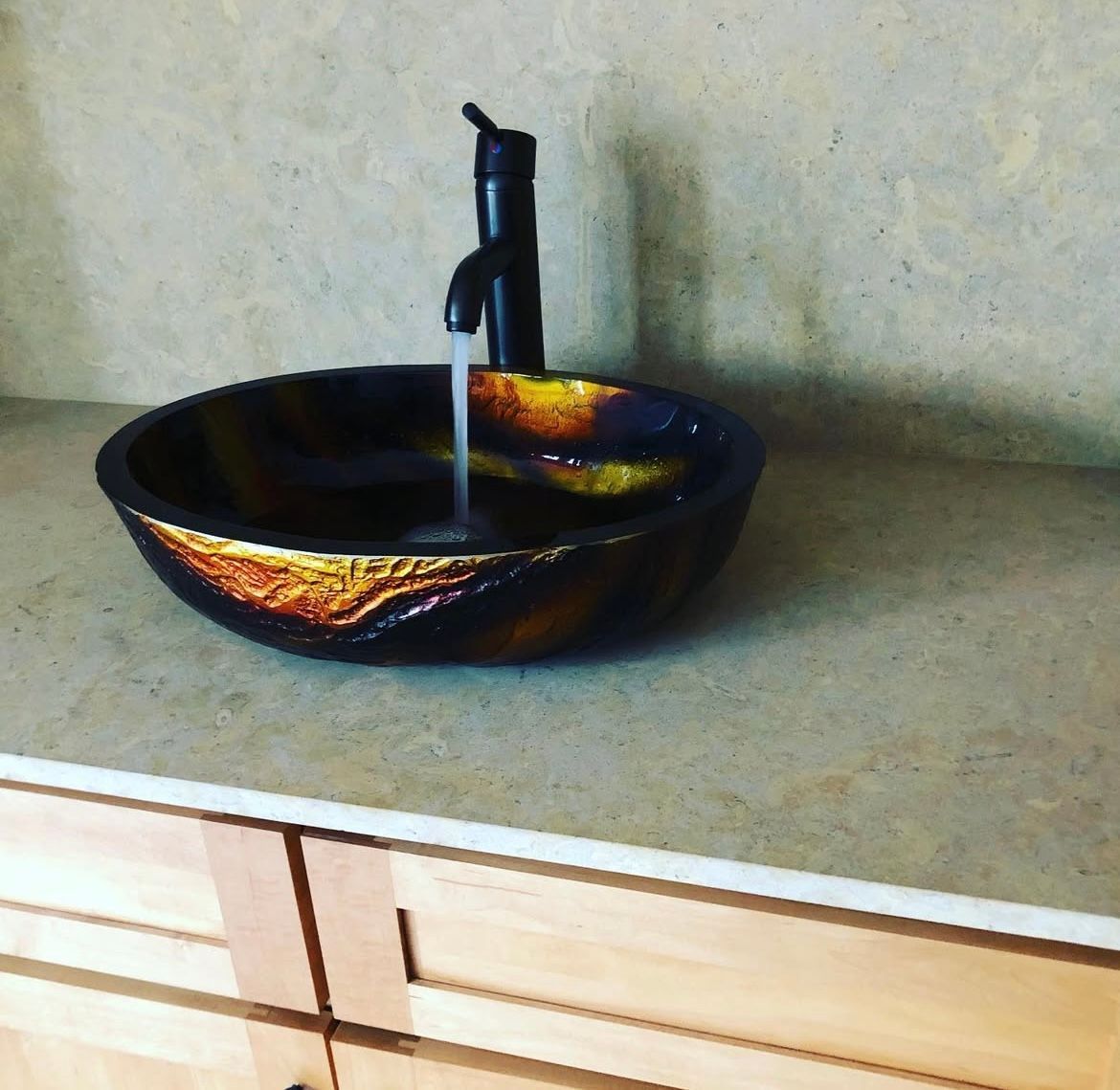 Dark, decorative vessel sink with running water, on a light countertop, next to a black faucet.