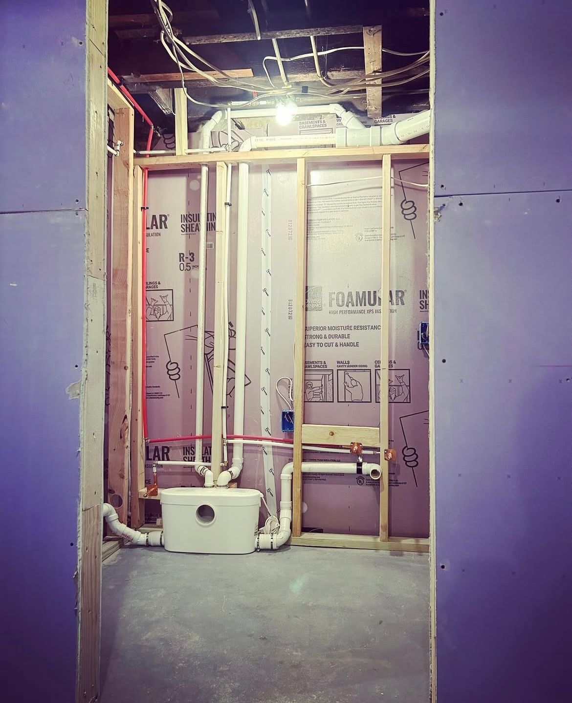 Interior view of a bathroom under construction, showing framing, plumbing, and insulation.