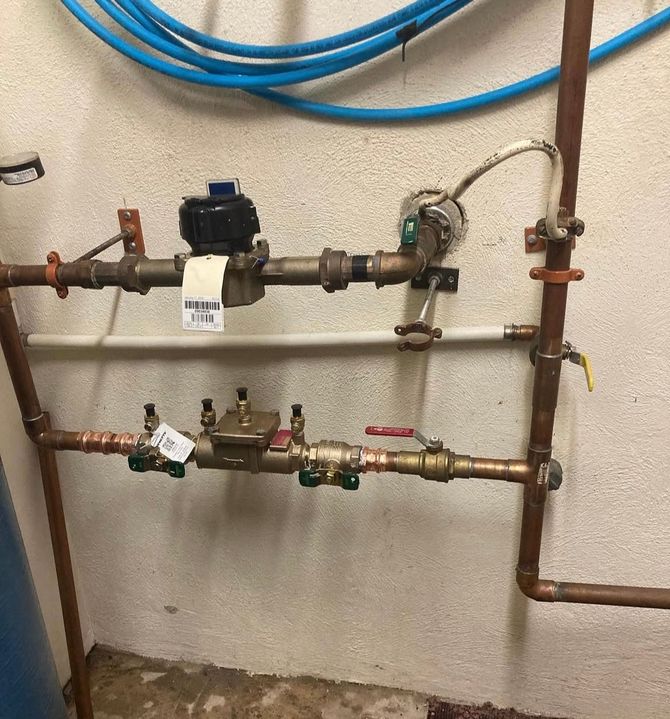 Plumber in overalls holding a white panel, working on a boiler with pipes and tanks in a utility room.