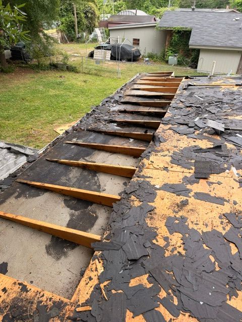 Damaged roof with exposed wood slats and torn black shingles in a suburban yard