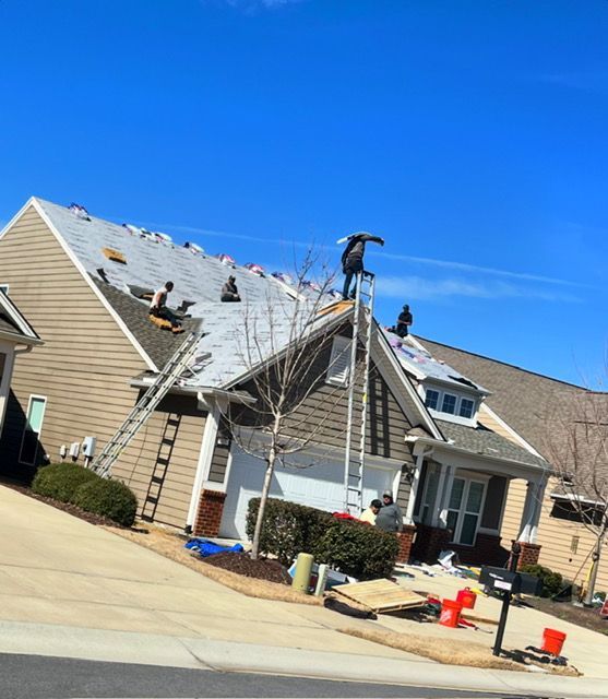 Damaged house roof with workers repairing shingles under a clear blue sky
