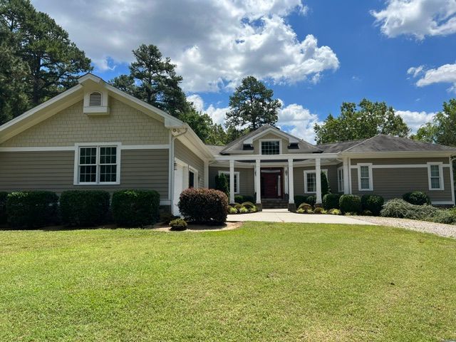 Single-story beige house with white columns, manicured lawn, and trees under a blue sky