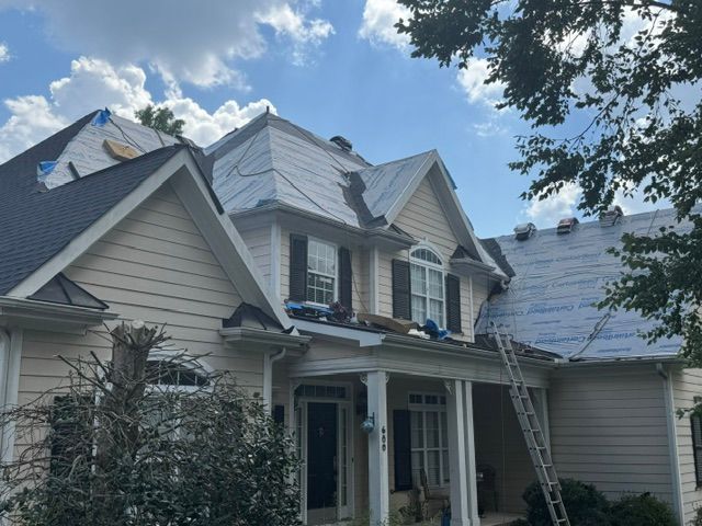 Two-story house with gray siding and roof, front porch, and a ladder leaning against the side.
