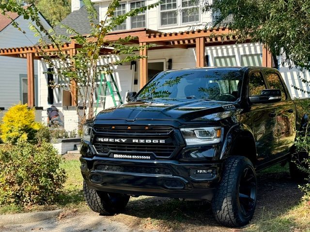 Black Ram pickup truck parked in a front yard beside a house and trellis-covered porch.