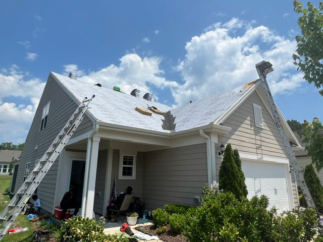 Damaged house roof under repair, with ladder and workers on a sunny day