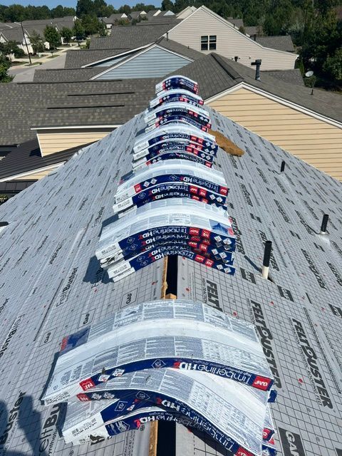 Roof under repair with rows of blue-and-white shingles and exposed underlayment on a steep house roof