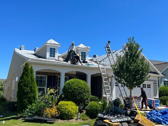 Workers repairing a house roof after storm damage, with ladders and materials in the front yard.