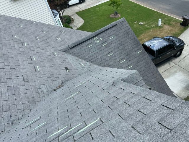 Roof shingles on a house with a driveway and parked black car below