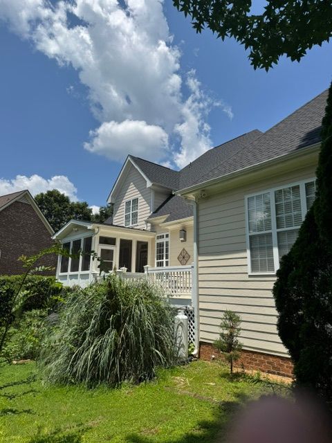 Suburban house exterior with beige siding, white trim, green lawn, and blue sky with clouds