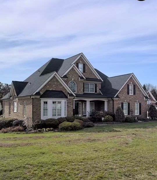 Large brick suburban house with gray roof, white trim, and front lawn under a blue sky