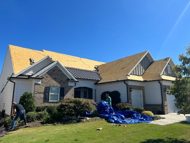 Worker covering house roof with blue tarp after storm damage