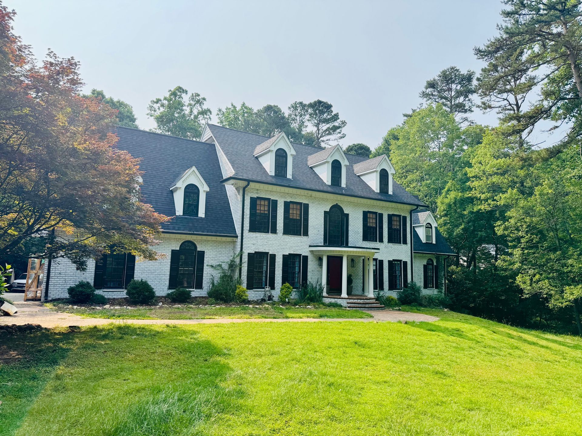 Large white country house with dark roof, green shutters, and a wide lawn in front