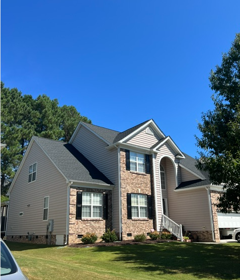 Suburban two-story brick and siding house with gray roof, front steps, and green lawn under a blue sky