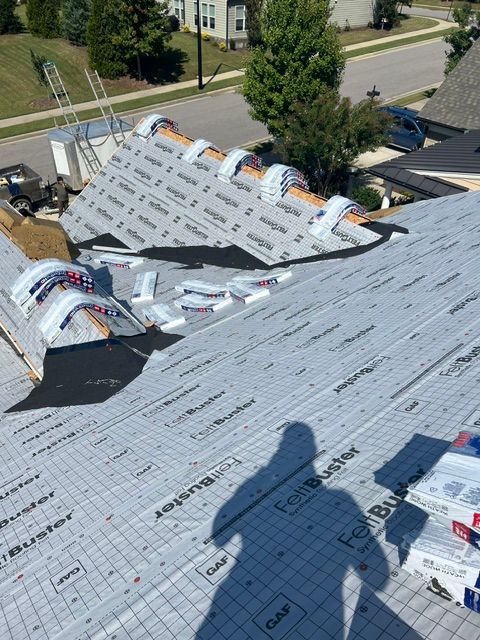 Roof under construction with silver underlayment, skylights, and a worker’s shadow in the foreground