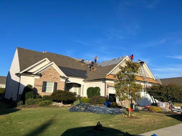 Suburban house roof being repaired by workers under a blue sky