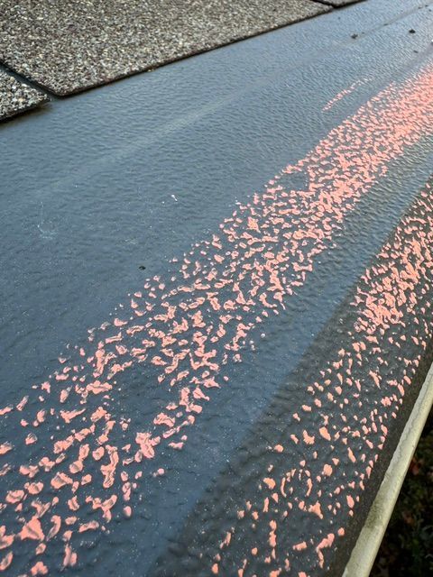 Black asphalt roof edge with a diagonal pink-speckled strip of granules near shingles