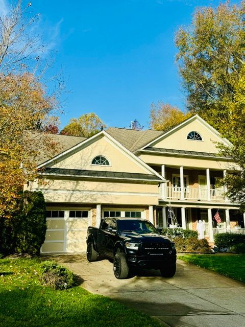 Two-story cream house with a black SUV in the driveway, surrounded by trees under a blue sky