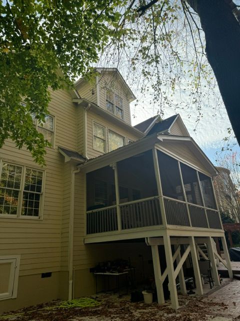 Two-story beige house with a screened porch and white support posts beneath leafy trees