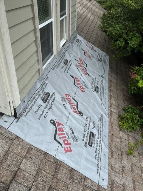 Roofing underlayment laid on a small sloped roof beside house siding and a window.