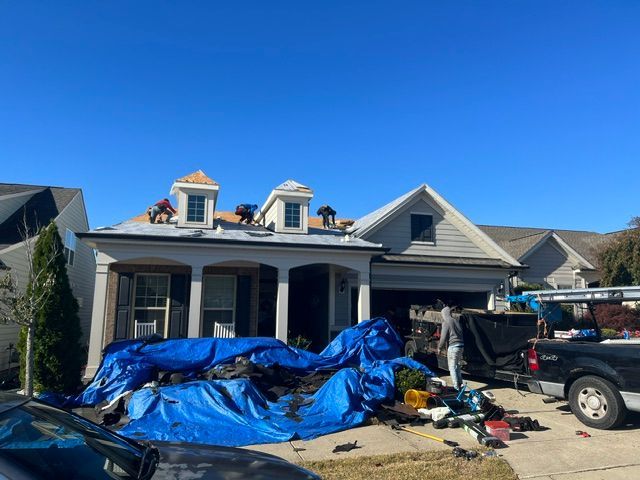 House exterior with debris-covered driveway and blue tarps under a clear sky