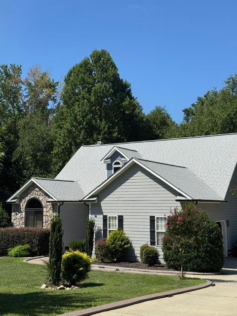 Suburban house with gray roof, white siding, manicured lawn, and trees under a clear blue sky