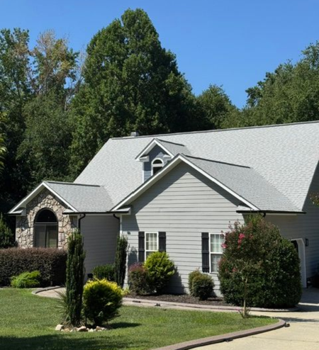 Suburban house with gray siding, white trim, a gabled roof, and a landscaped lawn under a clear blue sky