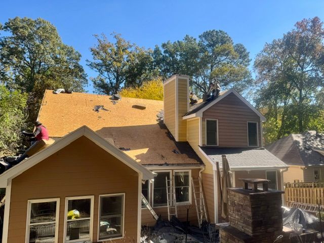 House roof being repaired, with workers and exposed roofing under a clear sky.