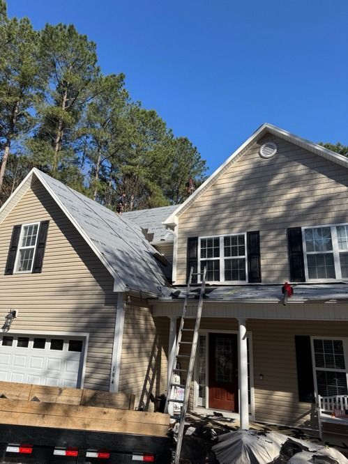Two-story beige house with roof damage and ladders set up for repairs
