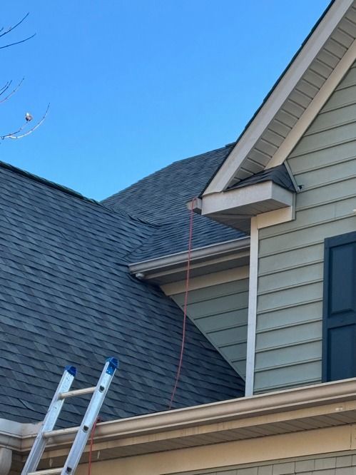 Roofing ladders beside a house with blue siding and a dark shingled roof under a clear sky