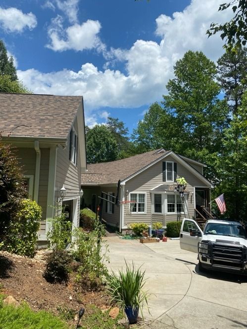 Suburban driveway with two houses, a black pickup truck, an American flag, and a blue sky with clouds