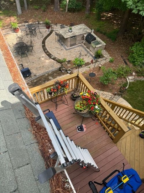 Backyard patio viewed from stairs, with wooden deck, grill, table, flower baskets, and umbrellaed seating area.